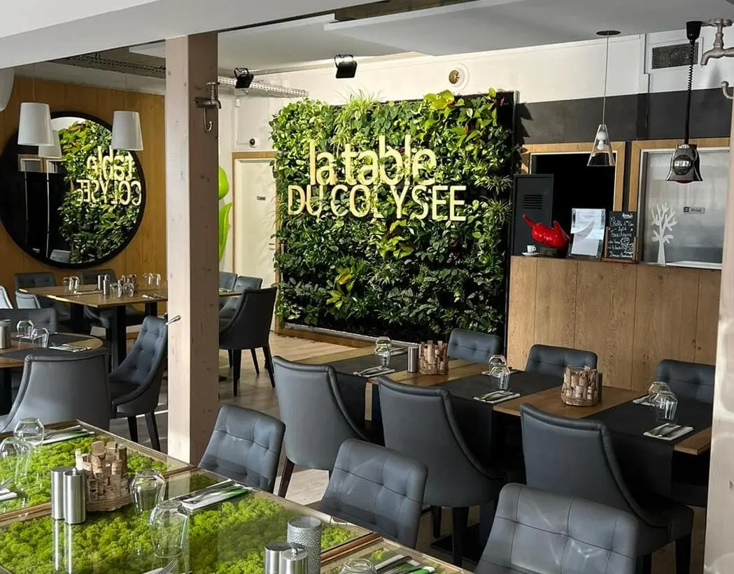 Vue sur un mur végétal naturel avec logo au second plan avec au premier plan des tables et des fauteuils